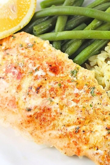 a piece of butter baked haddock on a white plate with rice pilaf, green beans and a lemon edge on the side.